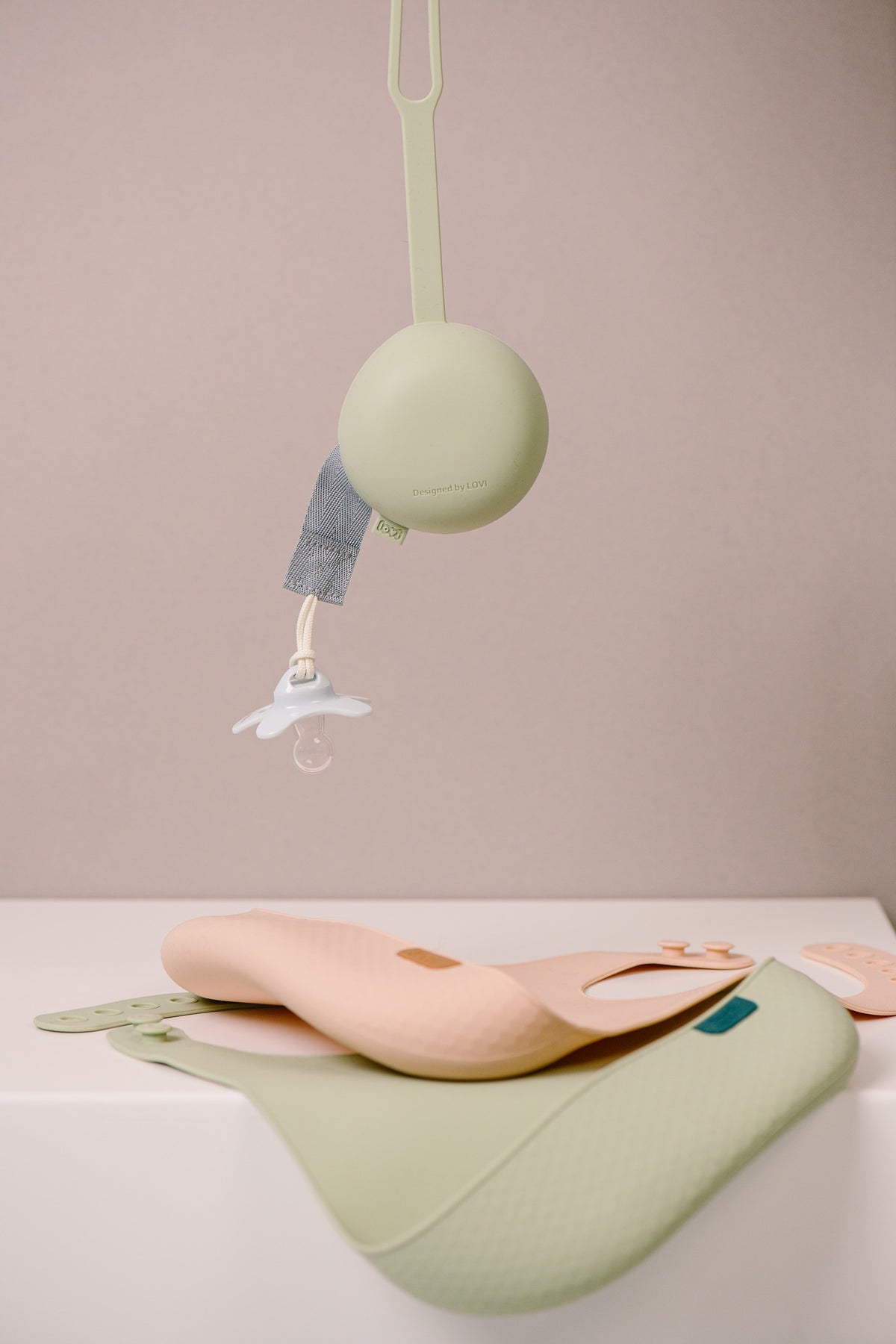 Difrax Lovi - Silicone Soother Holder - Pistachio Hanging & Silicone Bibs on Table