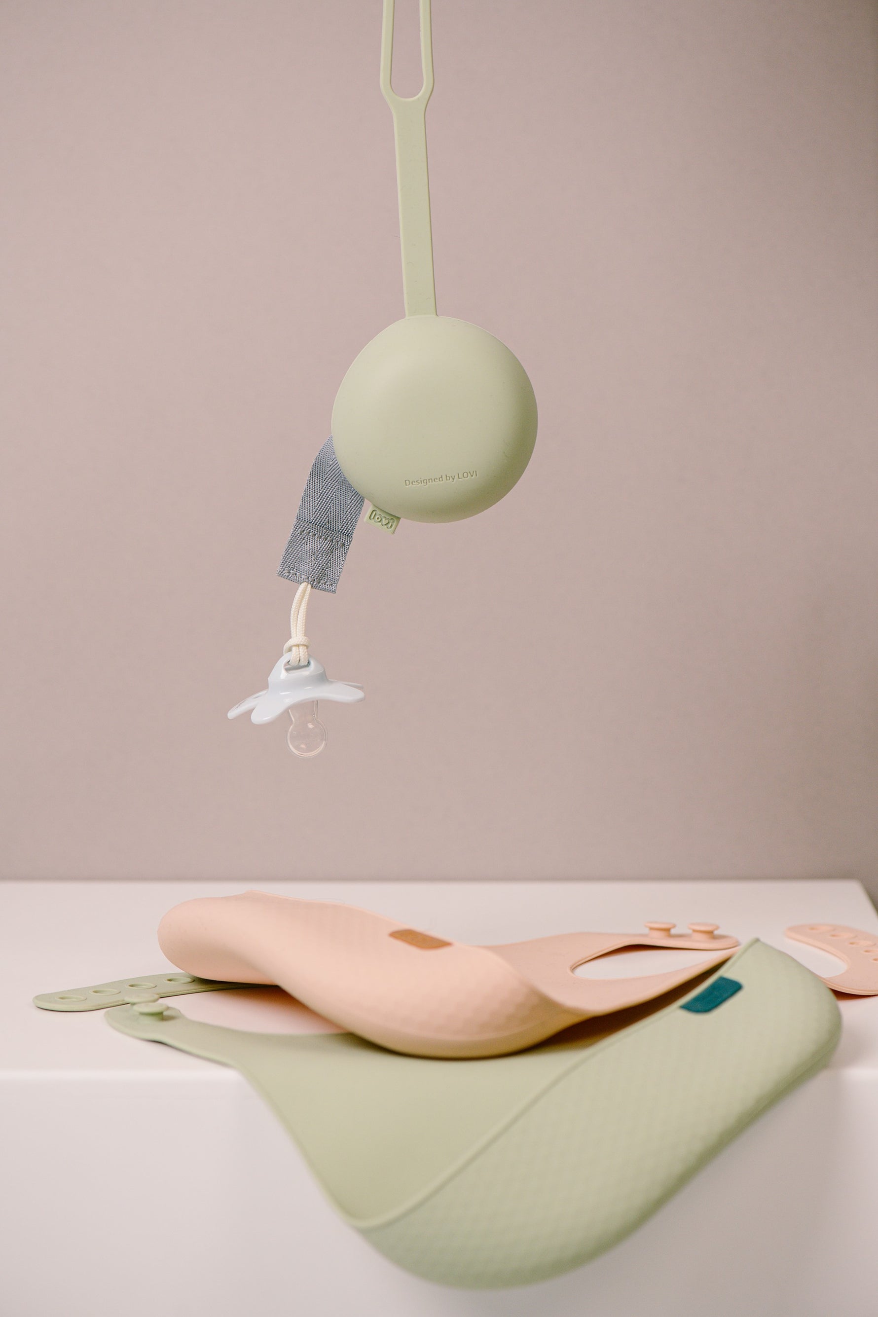 Difrax Lovi - Silicone Soother Holder - Pistachio Hanging & Silicone Bibs on Table
